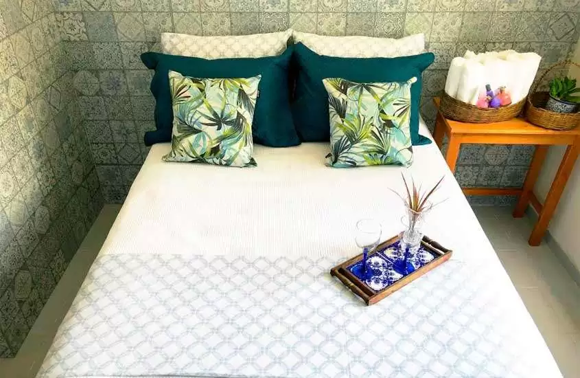 Quarto de uma das pousadas em Porto Seguro Bahia com preços baixos, cama de casal, toalhas, vaso de planta e tábua com taças e vaso decorativo