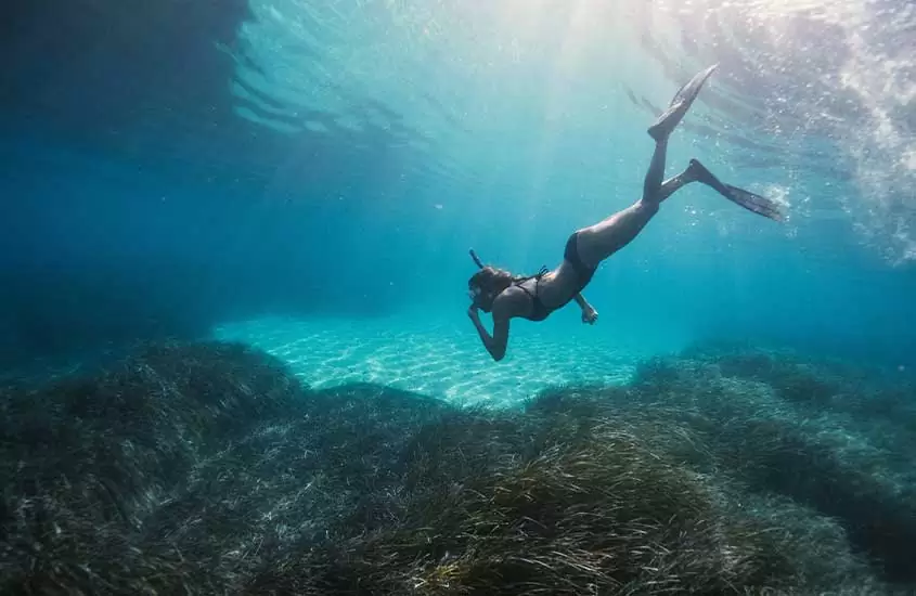 Mulher em um dos programas de o que fazer em Creta mergulhando de snorkel com algas ao redor e pedras no mar