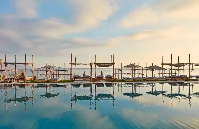 Em uma manhã de sol, área de lazer de um hotel em Creta com tendas de descano e piscina grande