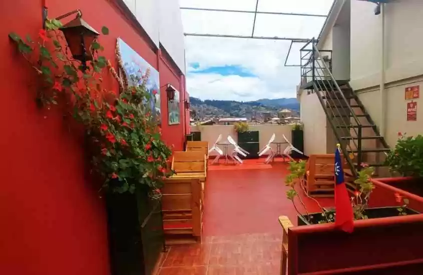 Em um dia de sol com nuvens, área externa de um dos melhores hostels em Cusco com mesas, cadeiras, plantas e vista da cidade