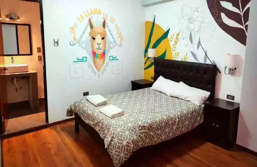 Quarto de hostel com pintura nas paredes, cama de casal, luminárias e um banheiro ao lado