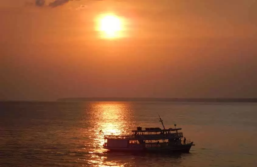 Durante o por do sol, rio em Manaus, lugar para viajar no feriado de corpus christi, com barco no meio e reflexo do sol na água