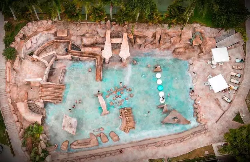 Visão aérea da área de lazer de um hotel fazenda perto de juiz de fora com piscina, esculturas de pedra, espreguiçadeiras e árvores ao redor
