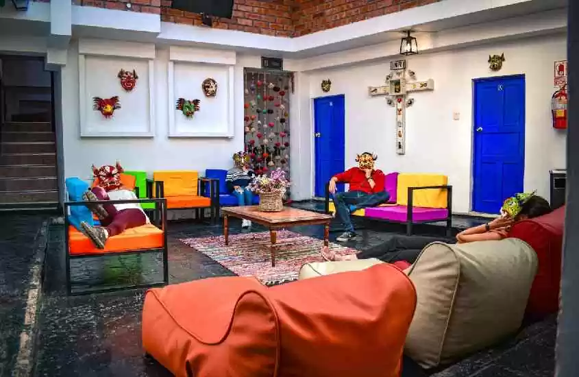 Lounge compartilhado de um dos melhores hostels em Cusco com puffs, sofás, poltronas, decorações nas paredes, mesa e tapete