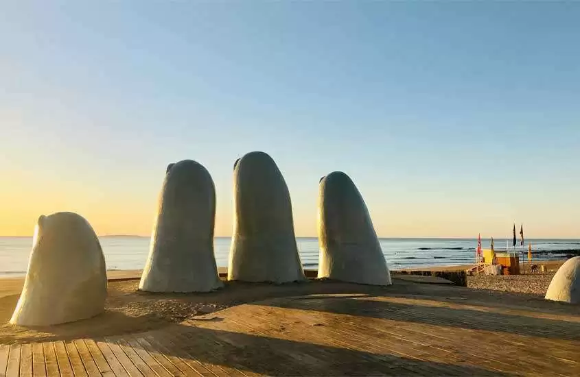 Em um dia de sol, monumento de Punta del Leste com praia na frente bandeiras e deck de madeira