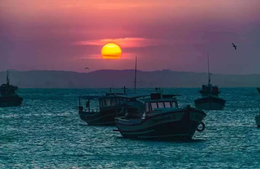 Durante o pôr do sol, mar de Búzios, um dos lugares para viajar no feriado de corpus christi com barcos e cidade no fundo
