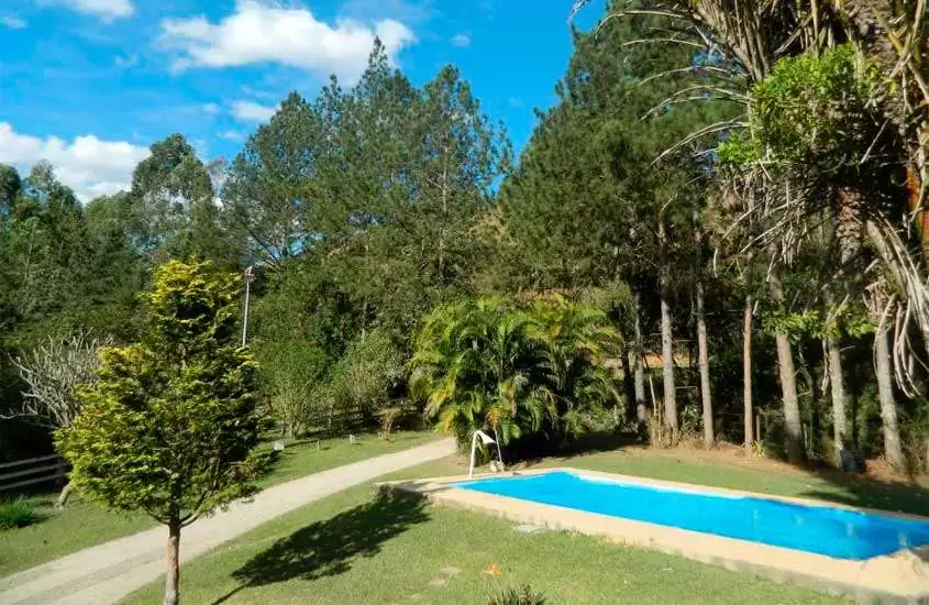 Em um dia de sol, área de lazer de um dos hotéis fazenda perto de juiz de fora com piscina, cascata, árvores e plantas ao redor
