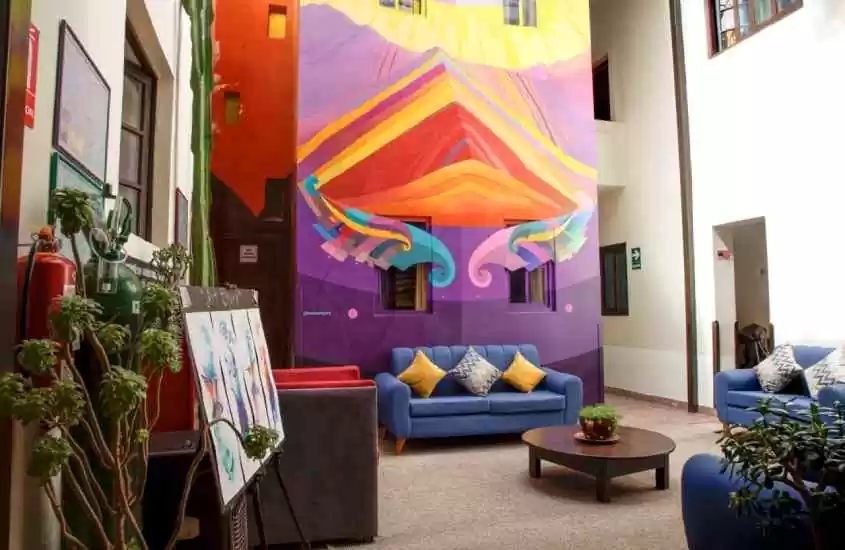 Área externa de um hostel em Cusco com sofás, pintura na parede, mesa e plantas decorativas