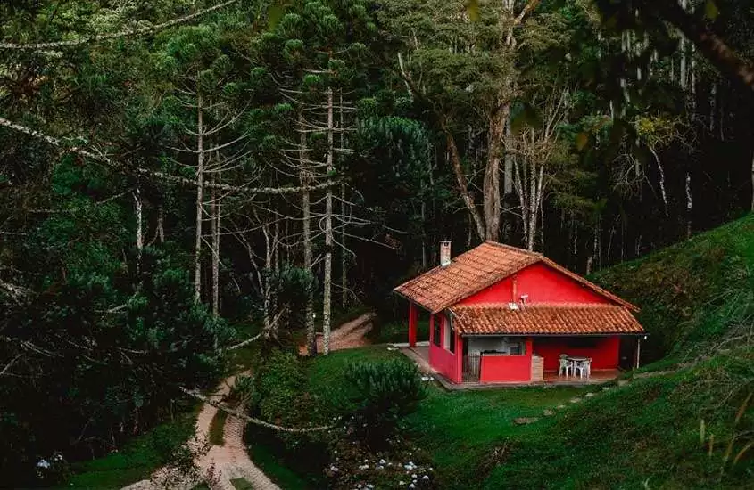 Em um final de tarde, casa vermelha em meio a natureza com diversas árvores ao redor