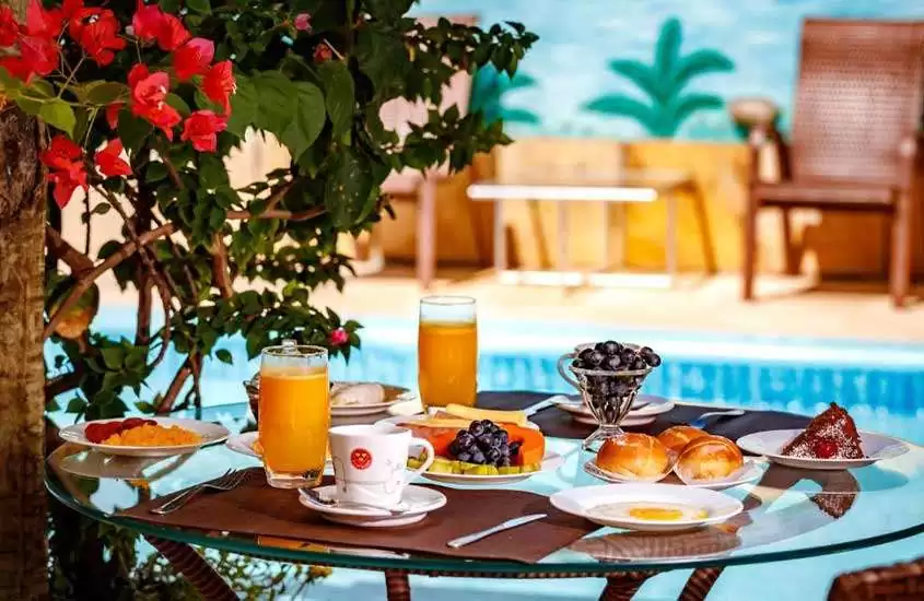 Em um dia de sol, mesa posta de café da manhã de um dos hotéis fazenda no ceara com piscina e plantas no fundo