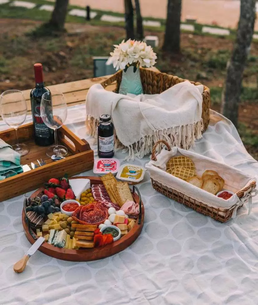 Mesa de picnic posta com frios, vinhos, geleiras, biscoitos, waffles e flores decorativas