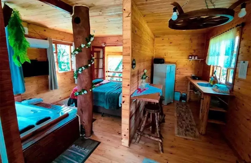 Interior de uma das cabanas na Serra Catarinense com cama, banheira de hidromassagem, cozinha, copa e móveis de madeira