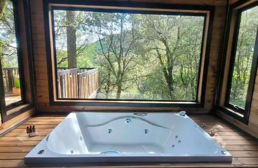 Banheira de cabana na serra catarinense com deck de madeira, janelas grandes com serra de paisagem