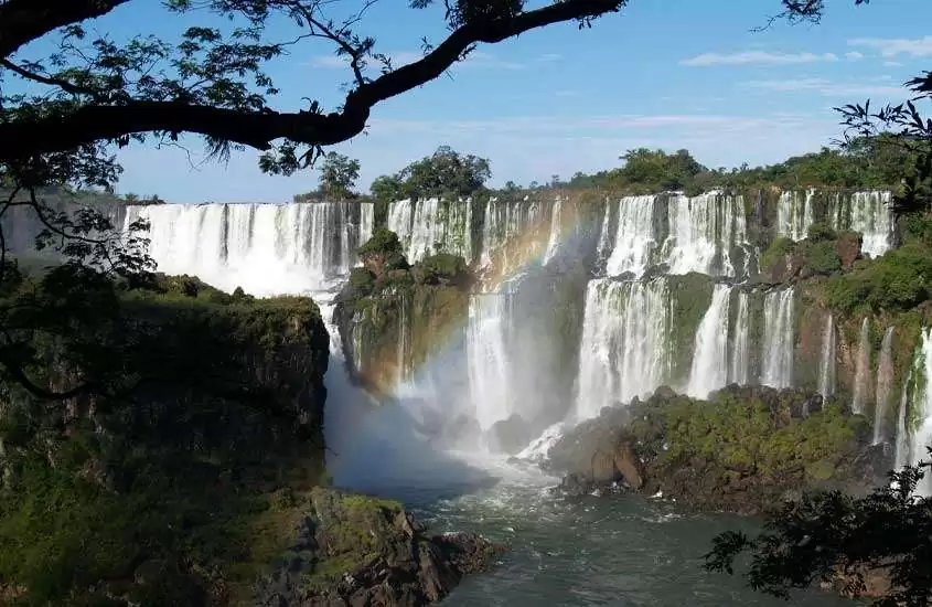 Em um dia de sol com arco-íris, paisagem das cataratas em foz do iguaçu com árvores, plantas e pedras ao redor