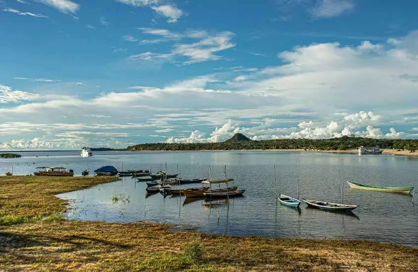 Em um dia de sol, paisagem de praia com barquinhos aportados e floresta atrás