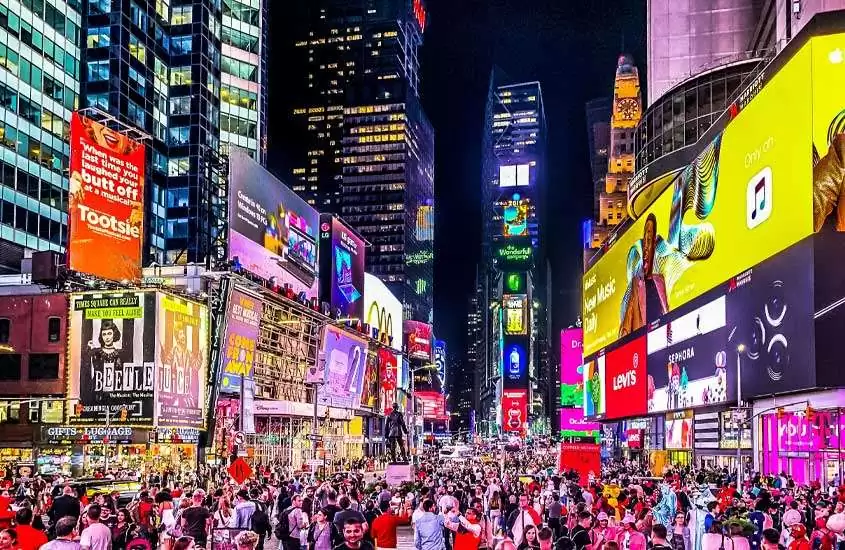 Durante a noite, rua de nova iorque, uma das cidades para passar o réveillon, iluminada por painéis luminosos com várias pessoas ao redor