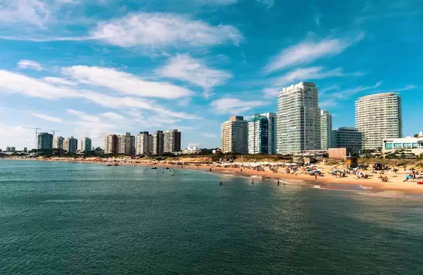 Em um dia ensolarado, paisagem panorâmica da praia com pessoas, guarda-sóis e prédios no fundo