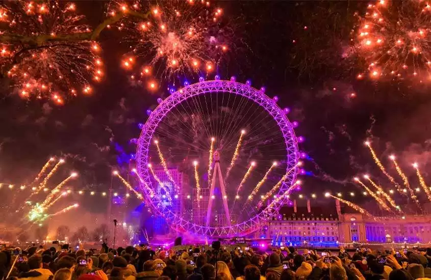 Durante a noite, queima de fogos com roda gigante iluminada, prédios atrás em Londres um ótimo lugar onde passar o réveillon