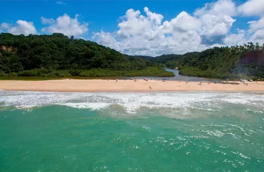 Em um dia de sol, praia de Porto Seguro, um dos lugares para passar o réveillon com pessoas, rio e árvores atrás